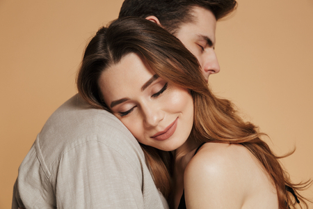 Portrait of a pretty loving couple hugging while standing isolated over beige backgroundの写真素材