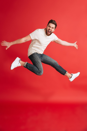 Image of excited emotional bearded man jumping isolated over red background wall looking camera.の写真素材