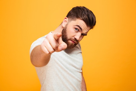 Portrait of a serious bearded man pointing finger at camera isolated over yellow backgroundの写真素材