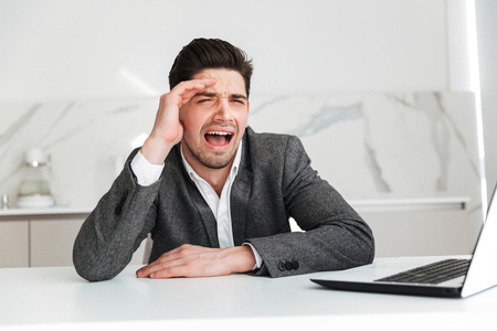 Portrait of mature male office worker sitting at table and crying and being disappointed because of business failureの写真素材