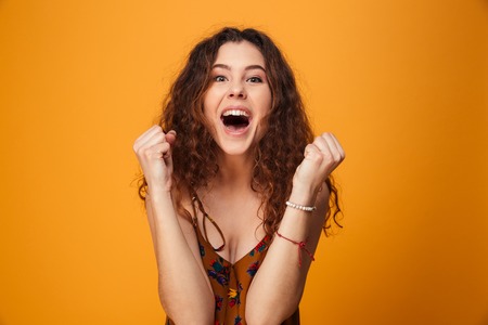 Picture of excited young lady standing isolated over yellow background. Looking camera make winner gesture.の写真素材