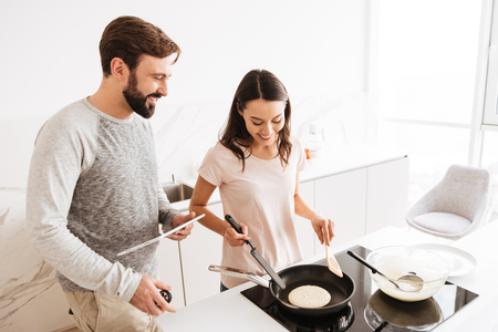 Cheerful young couple cooking pancakes together while standing at the stoveの写真素材