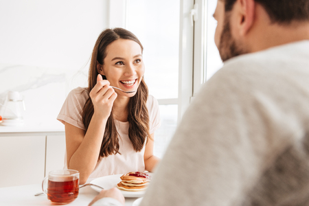 Cheerful young couple having breakfast while sitting together at the table on a kitchenの写真素材