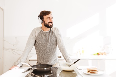 Portrait of a smiling young man cooking pancakes while listening to music with headphonesの写真素材