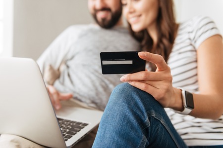 Close up portrait of a happy young couple shopping online while sitting on a couch with credit card and laptop computerの写真素材