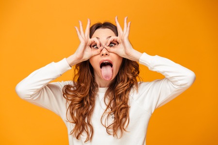Playful brunette woman in sweater holing arms on face like mask and looking at the camera over...