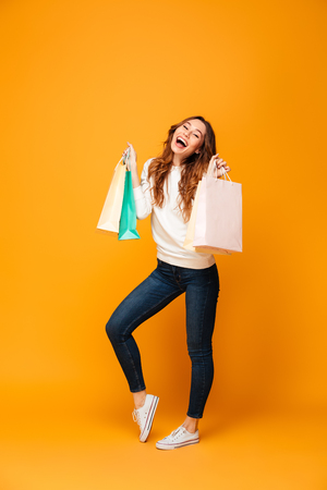 Full length image of Pleased brunette woman in sweater posing with packages and looking at the camera over yellow backgroundの写真素材