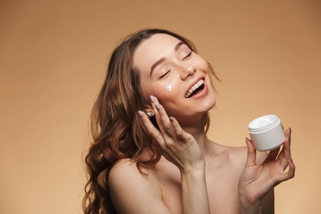 Photo of a gentle pretty young lady standing isolated with cream take care of her skin. Looking aside.の写真素材