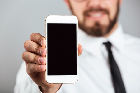 Close up of a businessman showing blank screen mobile phone isolated over gray backgroundの写真素材