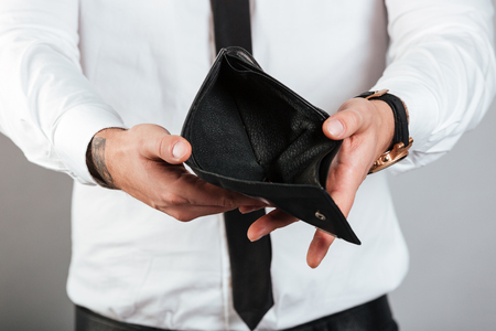 Close up of a poor man showing his empty wallet isolated over gray backgroundの写真素材