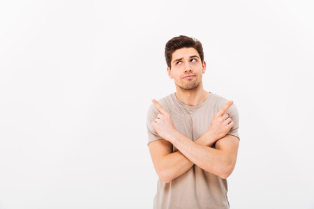 Image of muscular brooding man wearing beige t-shirt gesturing fingers aside with crossed arms on copyspace isolated over white backgroundの写真素材