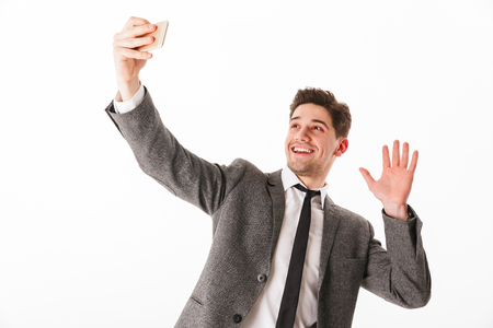 Portrait of a smiling young businessman taking a selfie isolated over white backgroundの写真素材