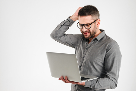 Image of confused businessman standing isolated over white background. Looking aside using laptop computer.の写真素材