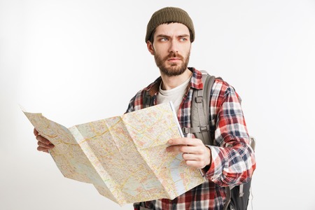Portrait of a concentrated bearded man in plaid shirt carrying backpack and holding guide map...