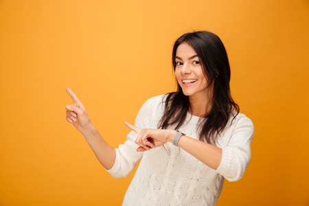 Portrait of a smiling young woman pointing fingers away at copy space isolated over yellow backgroundの写真素材