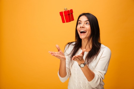 Portrait of a cheerful young woman catching small gift box isolated over yellow backgroundの写真素材