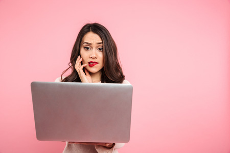 Image of beautiful woman 20s in casual clothing with interest watching at screen of silver notebook in her hands isolated over pink backgroundの写真素材