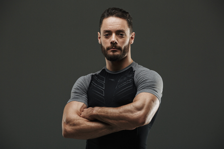 Portrait of a serious muscular sportsman standing with arms folded isolated over gray backgroundの写真素材