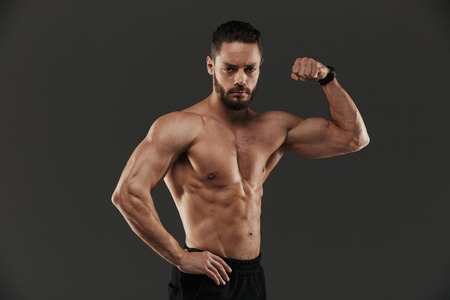 Portrait of a confident muscular bodybuilder flexing biceps isolated over gray backgroundの写真素材