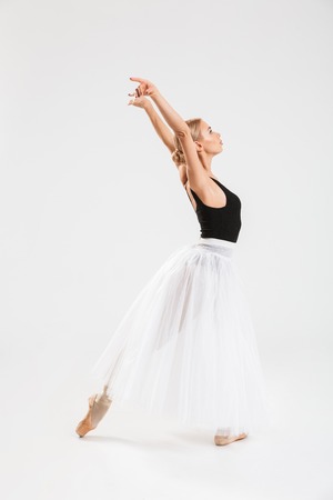 Full-lenght portrait of talented young woman ballerina dancing gracefully over white wall background isolated.の写真素材