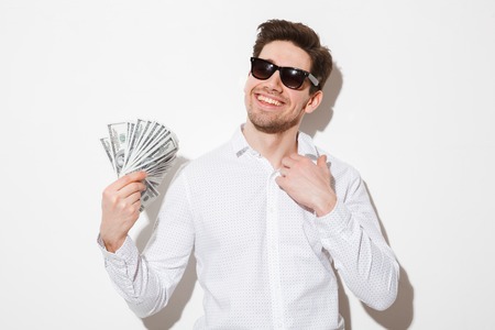 Portrait of a smiling young man in sunglasses holding money banknotes isolated over white backgroundの写真素材