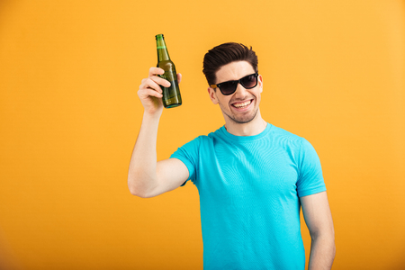 Portrait of a satisfied young man in sunglasses holding beer bottles isolated over yellow backgroundの写真素材