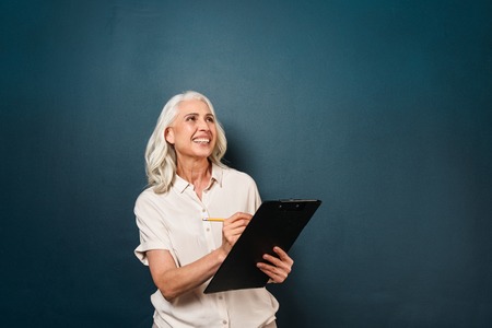 Image of happy smiling mature old woman isolated over dark blue background. Looking aside writing...