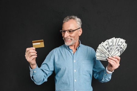 Portrait of a satisfied mature man dressed in shirt holding credit card while standing and showing...