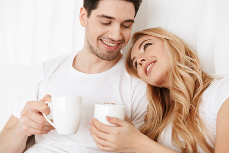 Image of young happy loving couple in bed indoors at home hugging and drinking tea.の写真素材