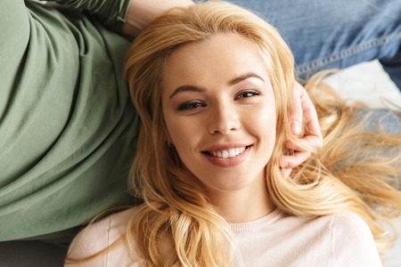 Photo of cute smiling young woman lies on her husband indoors at home. Looking camera.の写真素材