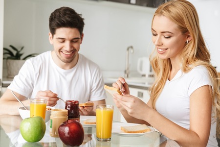 Portrait of a cheerful young couple in love having tasty breakfast while sitting at the table in a kitchenの写真素材