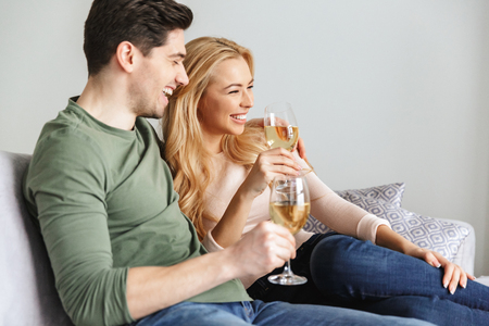 Picture of smiling young loving couple indoors at home drinking alcohol white wine champagne.の写真素材