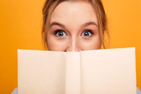 Photo of shocked young lady student standing isolated over yellow background covering face with...