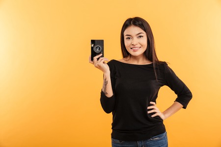 Image of cheerful young woman photographer standing isolated over yellow background holding camera.
