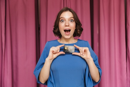 Image of young surprised excited woman shopaholic standing near changing room indoors looking camera...