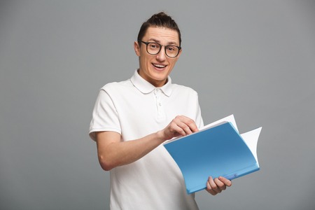 Photo of cheerful young man standing isolated over grey wall background. Looking camera holding...