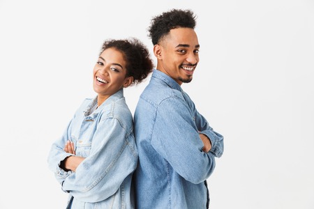 Happy lovely african couple in denim shirts standing back to each other while looking at the camera...