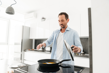 Smiling mature man cooking breakfast while standing at the kitchen at homeの写真素材