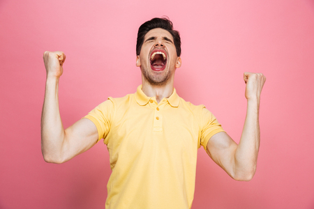 Portrait of a happy young man celebrating success and screaming isolated over pink backgroundの写真素材