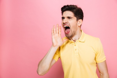 Portrait of an angry young man screaming loud isolated over pink backgroundの写真素材