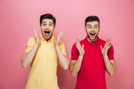 Portrait of an excited gay couple standing together with open mouths isolated over pink backgroundの写真素材