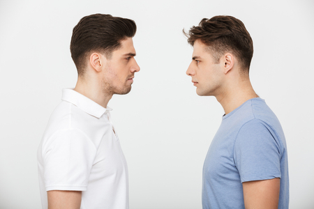 Full length portrait of two angry young men looking at each other isolated over white backgroundの写真素材