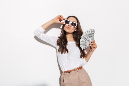 Portrait of a confident young asian businesswoman in sunglasses showing money banknotes and celebrating isolated over white backgroundの写真素材