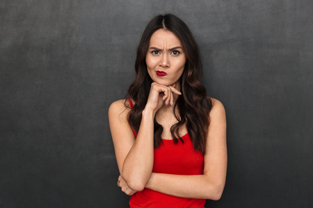 Serious pensive brunette woman in casual clothes reclines on arm and looking at the camera over black backgroundの写真素材