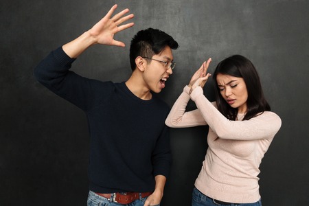 Worried asian woman covering himself while her boyfriend trying to kick her over black backgroundの写真素材
