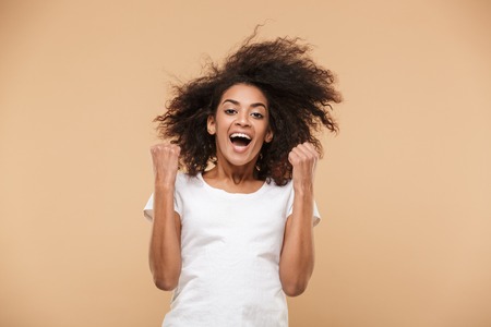 Portrait of a happy young african woman celebrating success isolated over beige backgroundの写真素材