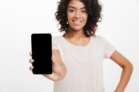 Beautiful woman with afro brown hair doing commercial and presenting new mobile device on camera isolated over white backgroundの写真素材