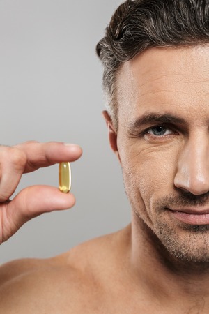 Cropped picture of of mature man standing isolated over grey wall background naked holding pill. Looking camera.の写真素材