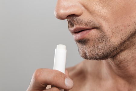 Cropped photo of of handsome mature man standing isolated over grey wall background naked holding lip balm.の写真素材