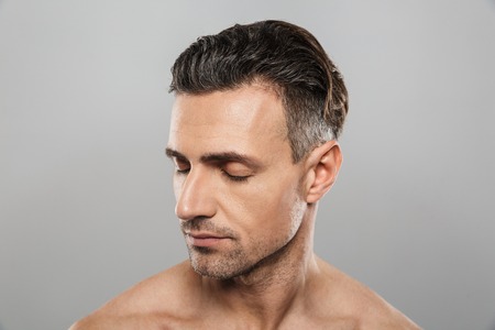 Image of handsome concentrated mature man standing isolated over grey wall background naked. Eyes closed.の写真素材